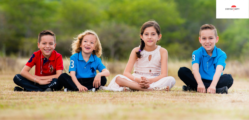 A row of 4 happy children sitting on the grass