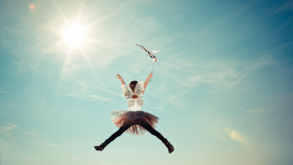 It is easy to exercise for happiness. A child dressed as a fairy leaps for joy against a blue sky.
